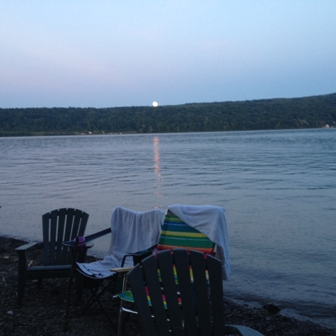 The full orange moon begins to rise over the Bluff and reflect upon the water.  Abandoned chairs hold wet towels.